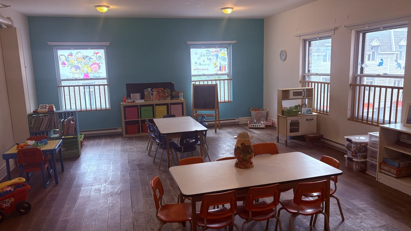 Salle d'activités avec tables, tableau noir et coin cuisinette